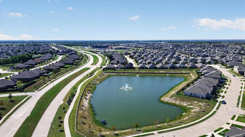 Residential neighborhood featuring numerous single-story homes, an expansive retention pond with a fountain, and paved roadways with sidewalks