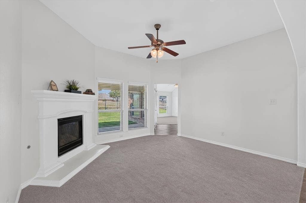 Vaulted ceiling, corner fireplace, recessed hearth, multiple windows, and a ceiling fan with integrated lighting