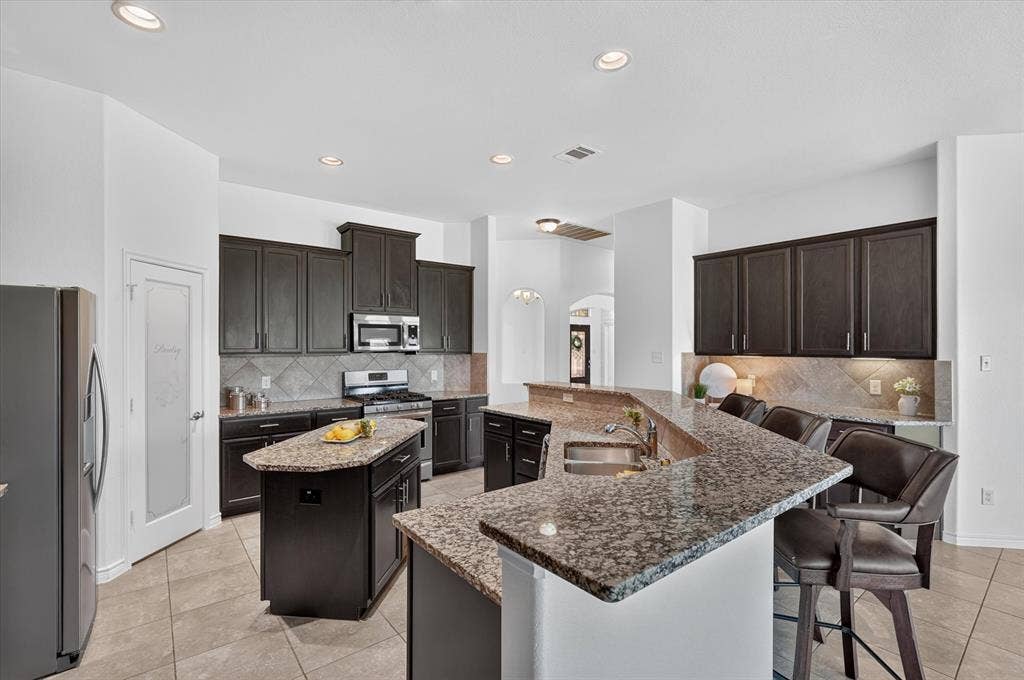 Kitchen featuring dark wood-finish cabinetry, granite countertops, stainless steel appliances, and a central island