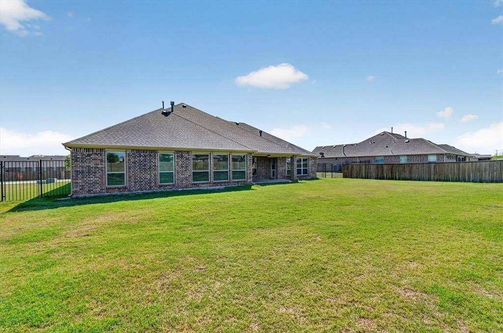 Expansive green lawn with a brick exterior, multiple windows, and a black metal fence