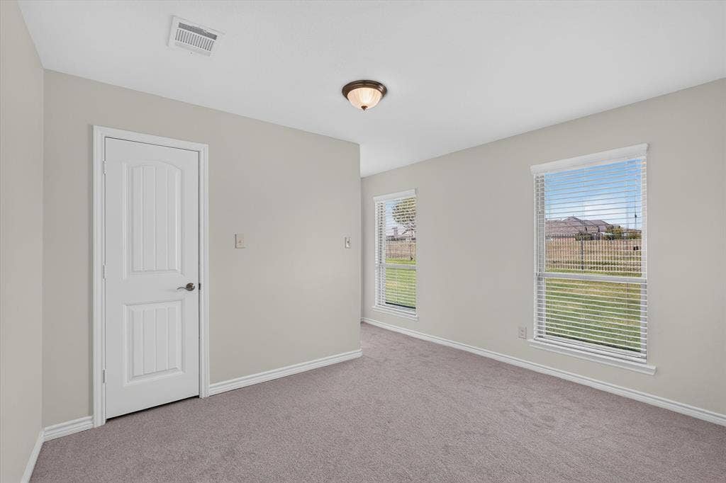 Soft gray carpeting with white baseboards, two windows with blinds, a white paneled door, and a flush mount ceiling fixture