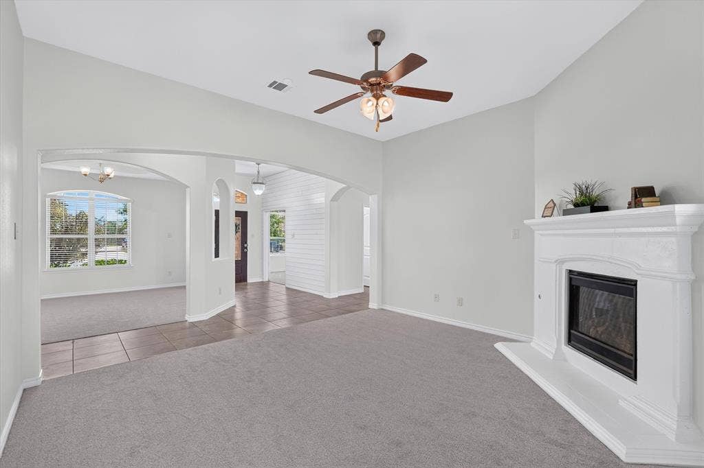 Central living space with vaulted ceilings, a ceiling fan, a fireplace with a white mantel, and arched doorways