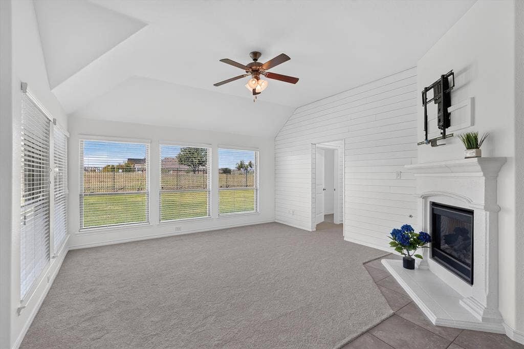Vaulted ceiling, ceiling fan, fireplace with mantel, window blinds, and shiplap accent wall