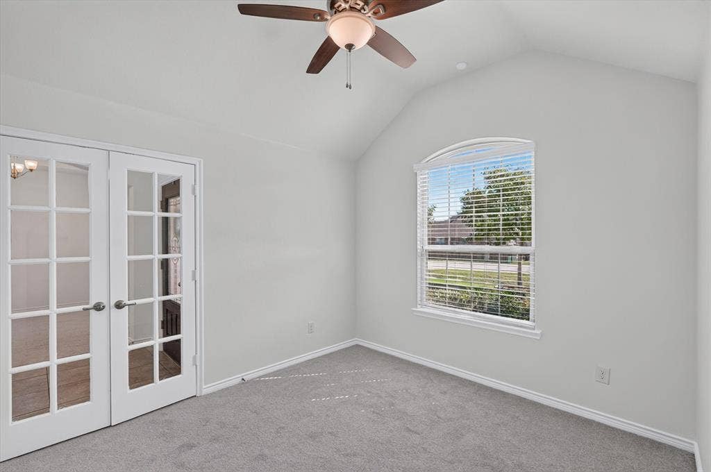 Vaulted ceiling featuring a ceiling fan with integrated lighting, arched window, French doors, and neutral carpeting