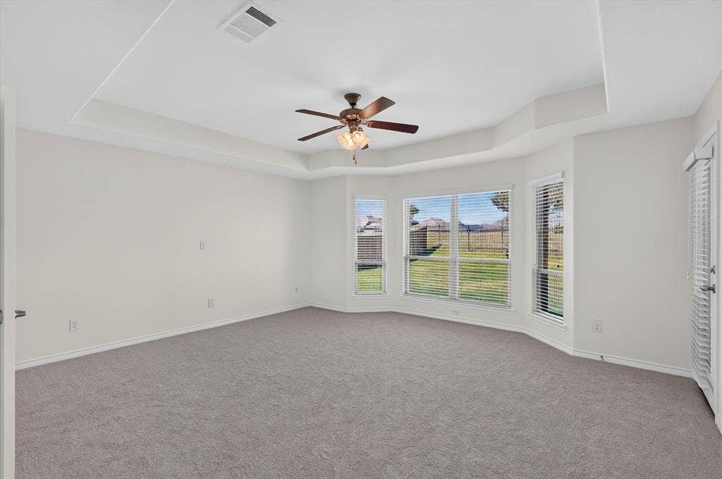 Tray ceiling with a ceiling fan, bay window configuration, and gray carpeting