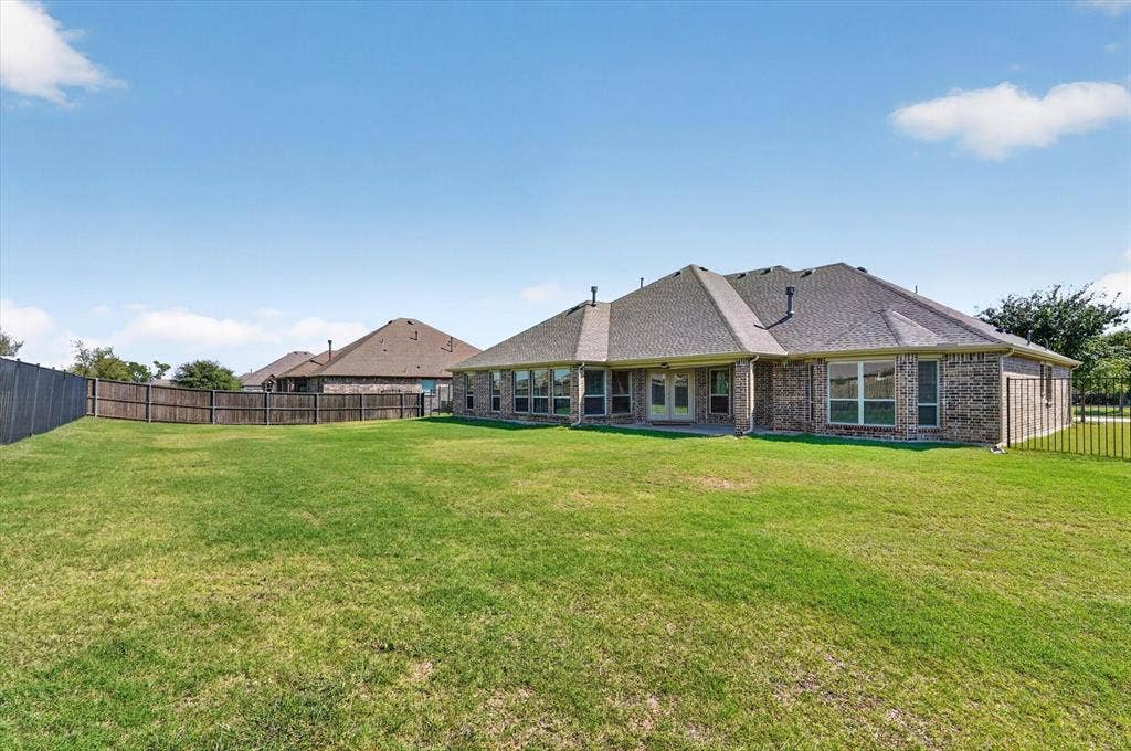 Expansive grass lawn with a full privacy fence and brick exterior