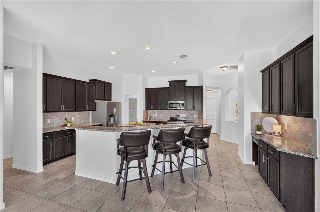 Expansive kitchen featuring dark wood cabinetry, granite countertops, tile backsplash, and recessed lighting