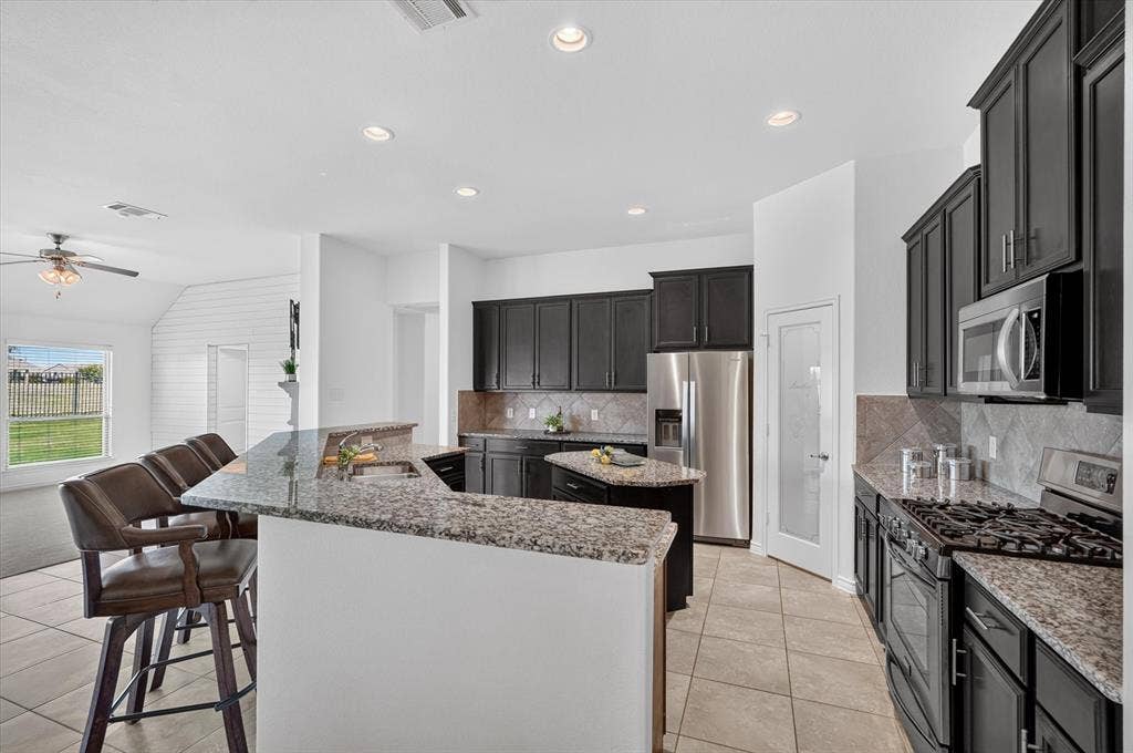 Kitchen featuring dark cabinetry, granite countertops, stainless steel appliances, and a tiled backsplash