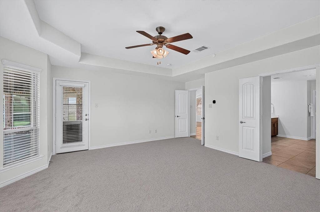 Tray ceiling with a ceiling fan, light gray carpeting, glass-paneled exterior door, and multiple interior doorways
