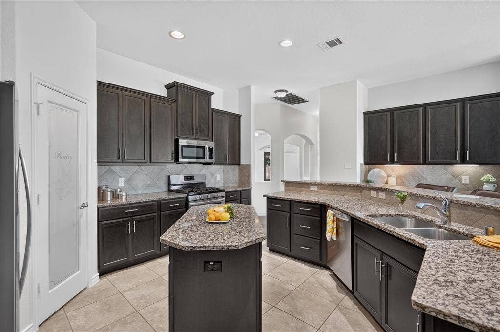 Kitchen featuring dark wood-finish cabinetry, granite countertops, stainless steel appliances, a tiled backsplash, and recessed lighting