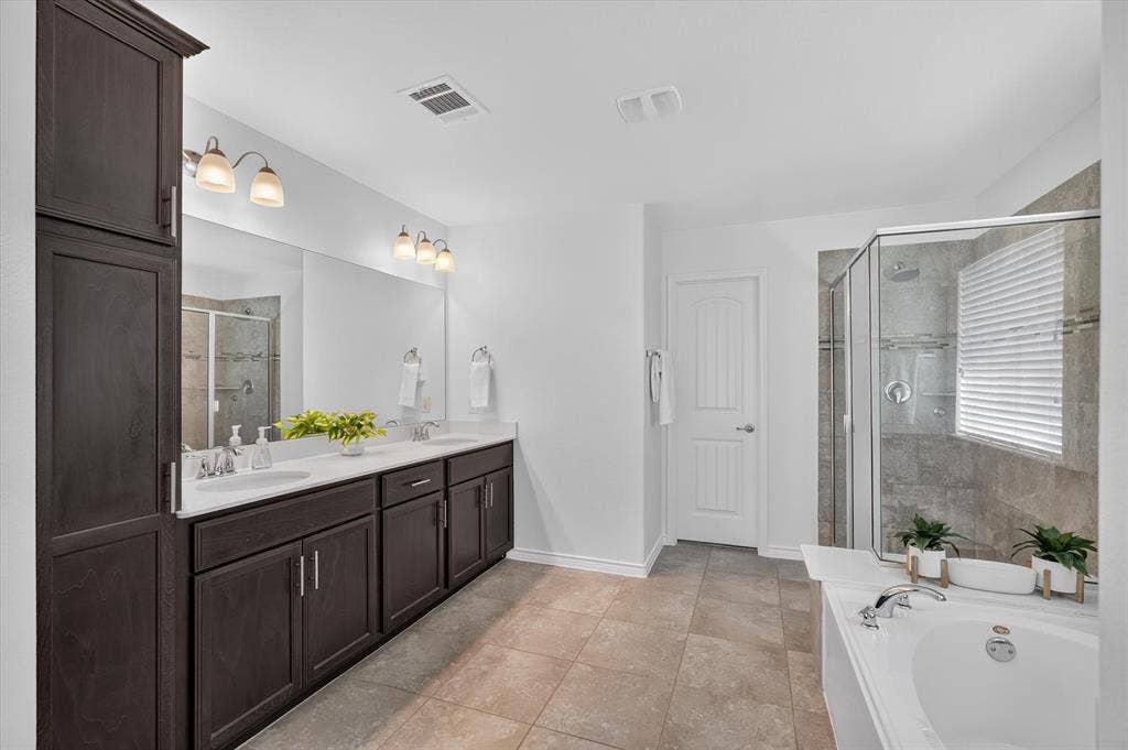 Dual vanity with white undermount sinks, dark wood-finish cabinetry, built-in storage cabinet, enclosed glass shower, and a built-in soaking tub