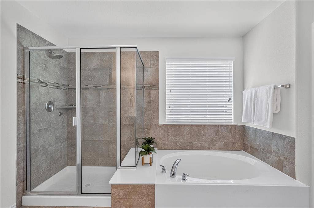 Walk-in shower with clear glass enclosure and built-in shelving, accompanied by a corner soaking tub with deck-mounted fixtures