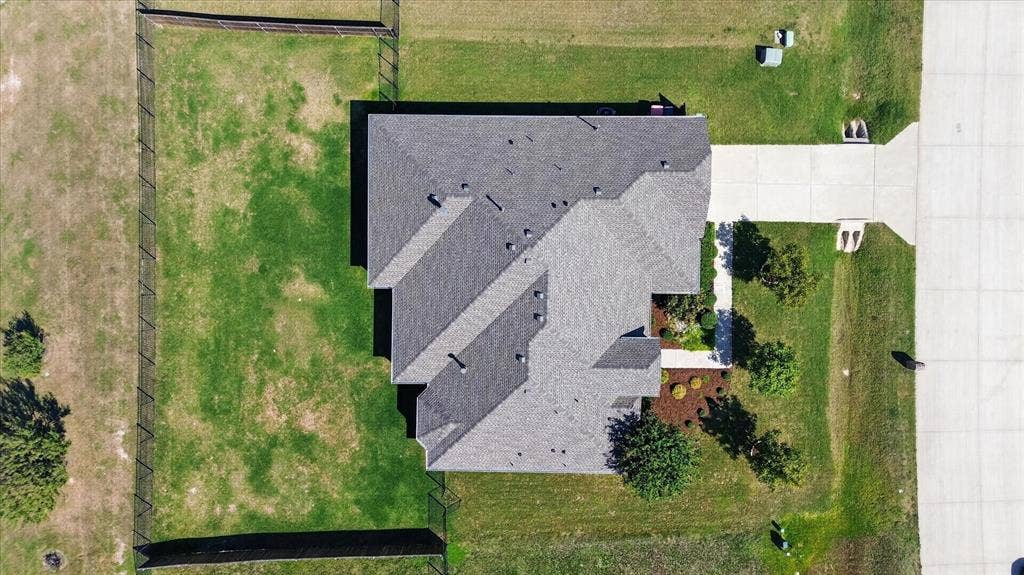Gable roof design with multiple pitch angles, concrete driveway, fenced property perimeter, and landscaped front entry with mature plantings