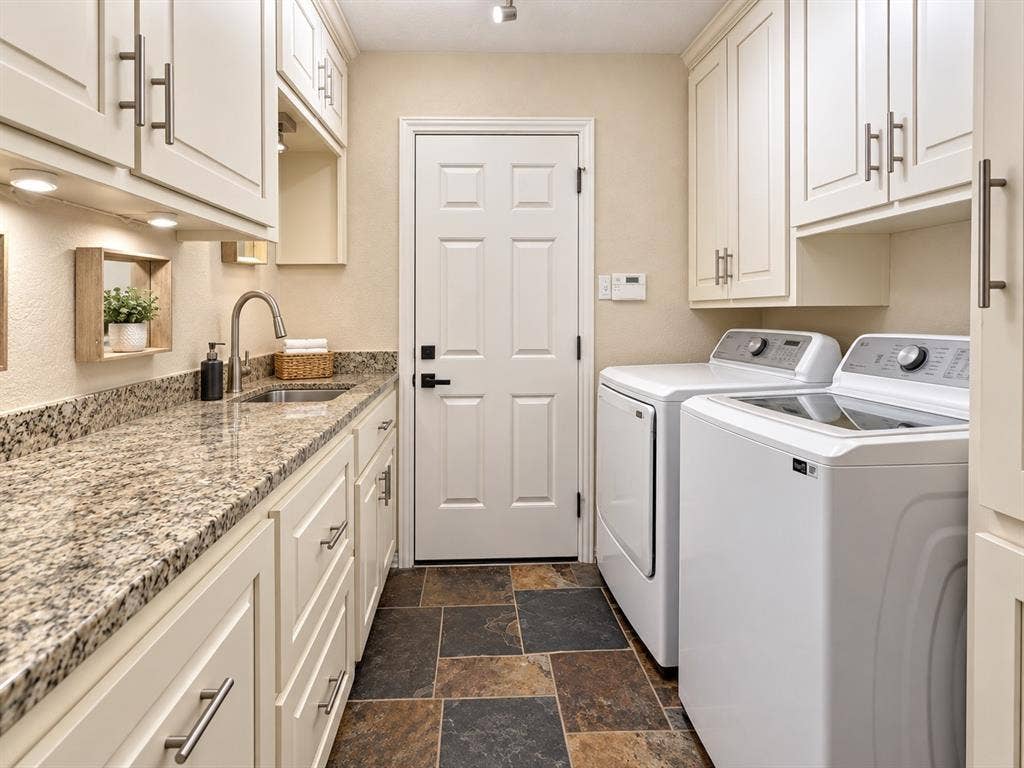 2912 Meadow Glen Drive, Flower Mound, TX 75022 Laundry room featuring extensive white cabinetry, a stainless steel sink, granite countertops, and slate tile flooring