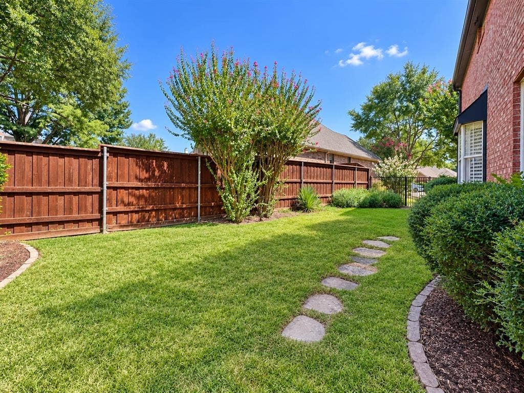 2912 Meadow Glen Drive, Flower Mound, TX 75022 Expansive lawn with a stepping stone pathway, complemented by a wood privacy fence and established landscaping