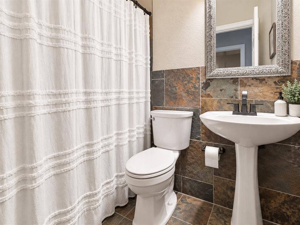 2912 Meadow Glen Drive, Flower Mound, TX 75022 Pedestal sink with a matte black faucet, wall-mounted mirror, and multi-toned tile wainscoting