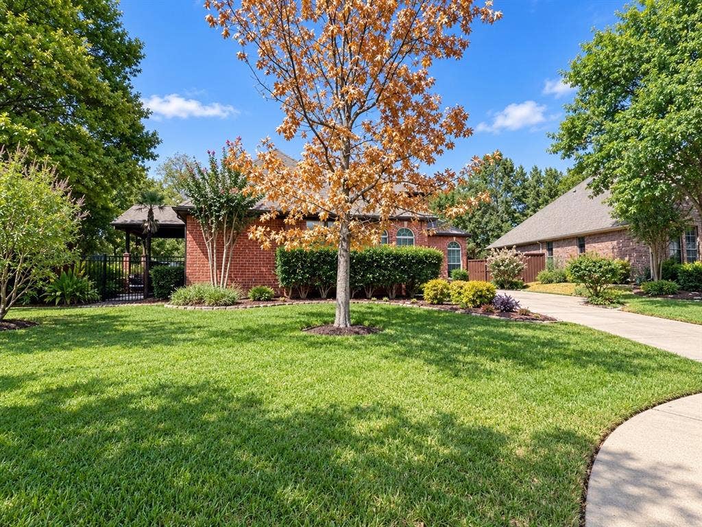 2912 Meadow Glen Drive, Flower Mound, TX 75022 Brick exterior residence with arched windows, an attached two-car garage, mature landscaping, and a fenced side yard with a pergola