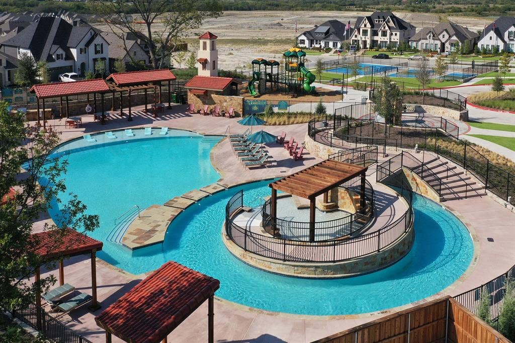 1411 Potenza Road, Fate, TX 75087 Community swimming pool featuring a central island with a wood-beam pergola, stone retaining walls, tiled pool decking, and adjacent play structure