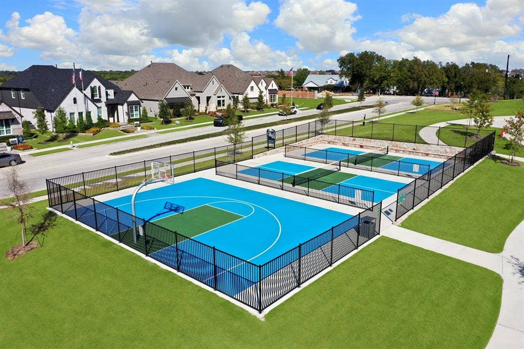 1411 Potenza Road, Fate, TX 75087 Recreational area featuring a basketball court and multiple pickleball courts enclosed by black metal fencing, set within a landscaped lawn area