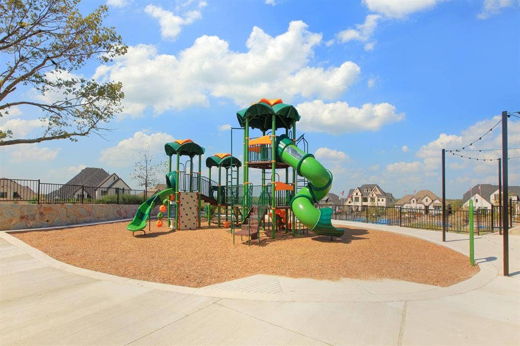 1411 Potenza Road, Fate, TX 75087 Recreational area featuring a multi-level playground structure, spiral slide, rock-climbing panel, wood-chip ground covering, and decorative string lighting