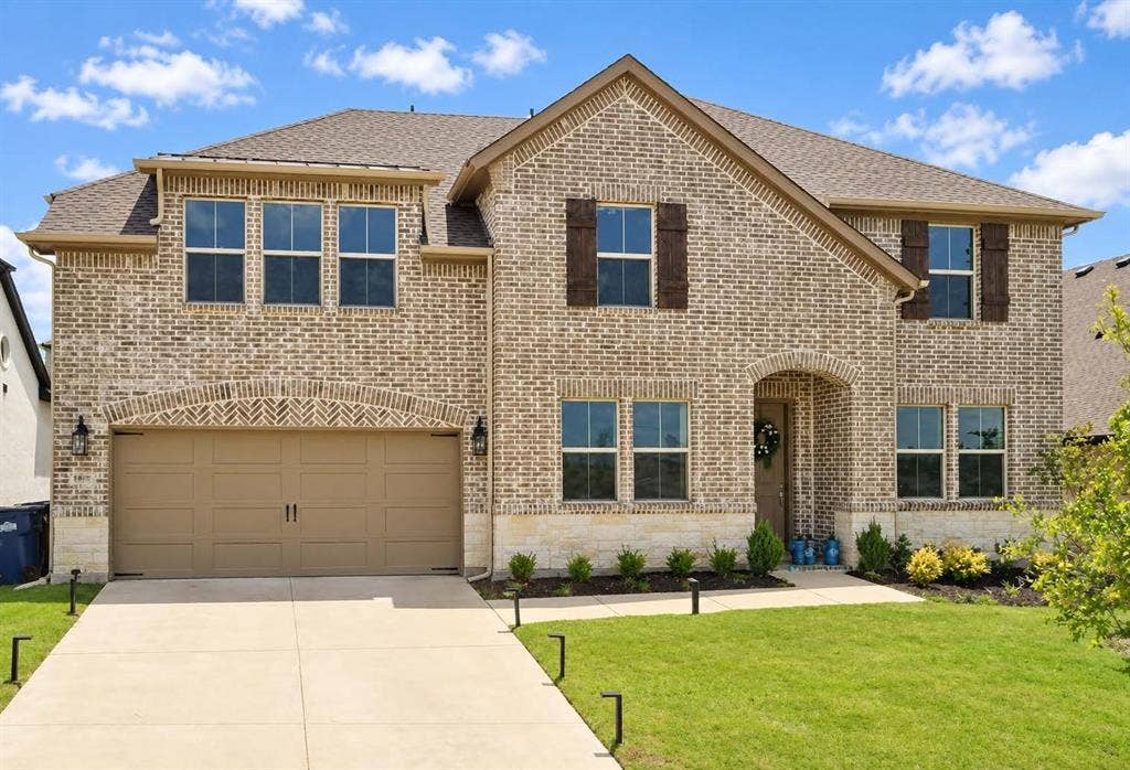 1411 Potenza Road, Fate, TX 75087 Brick exterior with stone accents, covered front entry, attached two-car garage, multiple windows, and mature landscaping