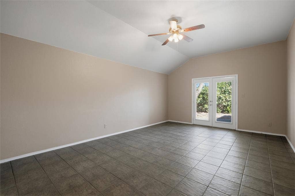 Vaulted ceiling with an attached ceiling fan, dual-pane French doors, and tile flooring