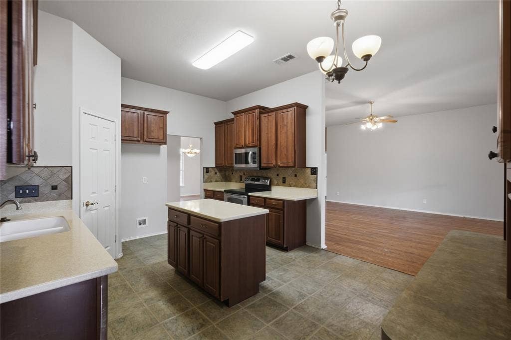 Kitchen featuring a central island, wood-finish cabinetry, light-toned countertops, tile flooring, and stainless steel appliances
