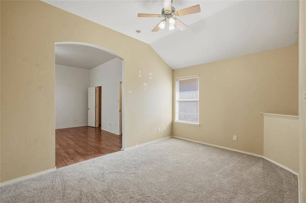 Vaulted ceiling with an attached ceiling fan, arched doorway, window with blinds, and carpeted flooring