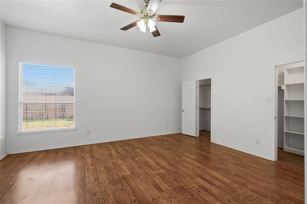 Spacious room featuring wood-finish flooring, a ceiling fan, and two closet spaces with built-in shelving