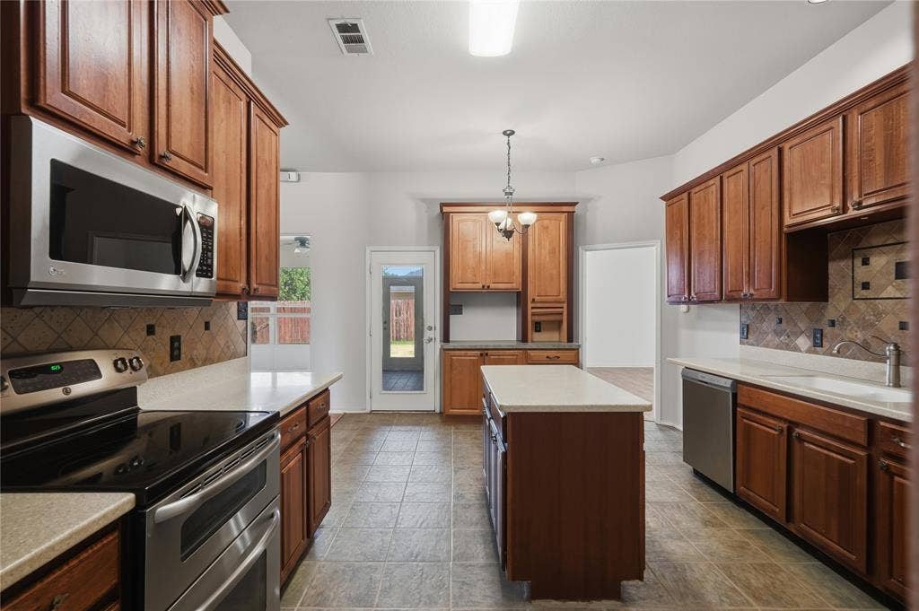 Kitchen featuring wood cabinetry, stainless steel appliances, a center island with countertop, tile flooring, and a tiled backsplash