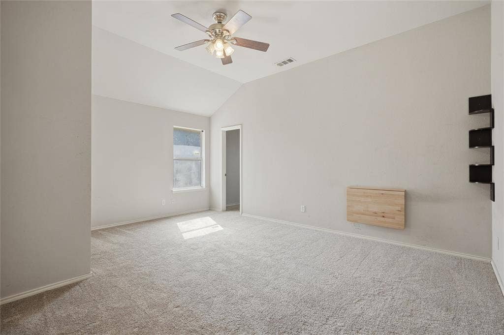 Vaulted ceiling with a ceiling fan, light-colored carpet flooring, and a window for natural light