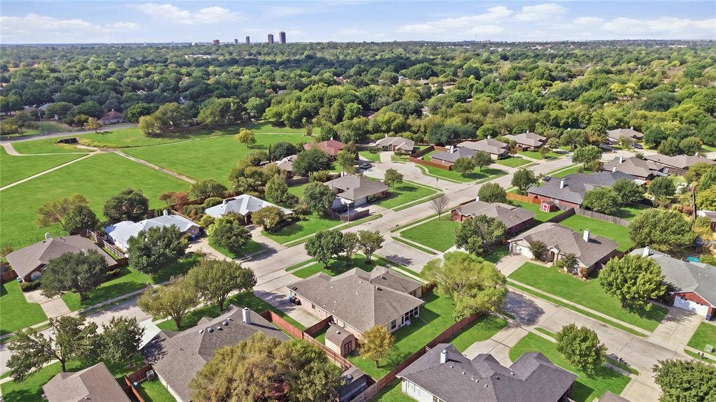 Expansive green spaces and mature trees surround residential properties, featuring paved streets and varied rooflines