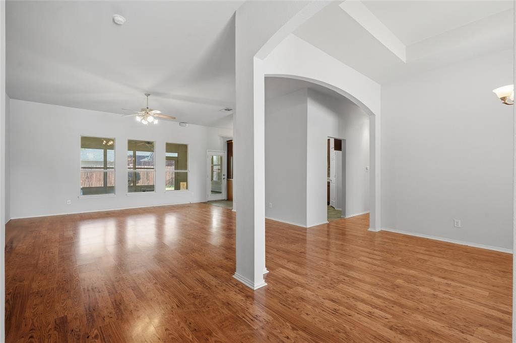 Wood-finish flooring throughout, multiple windows, archway entry, and ceiling fan with integrated lighting