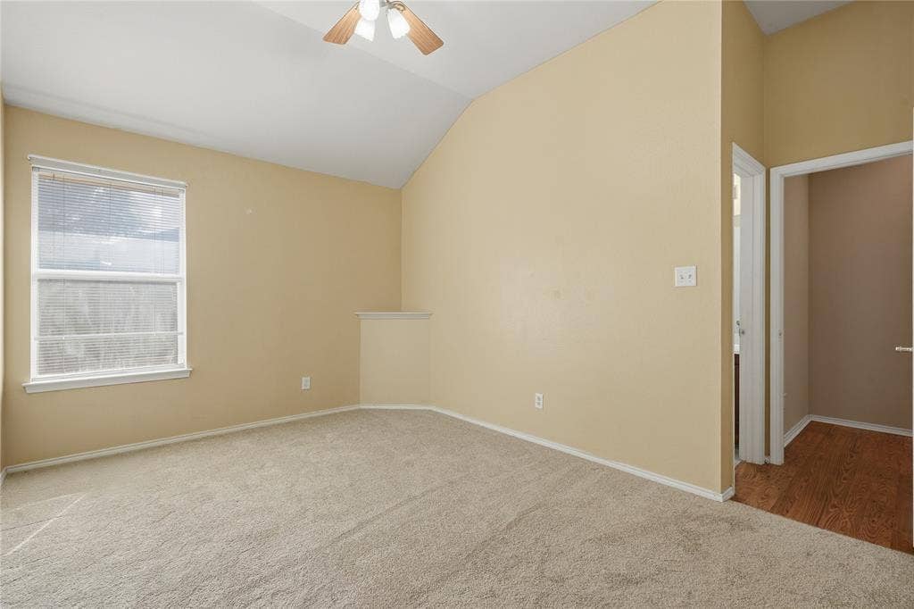 Vaulted ceiling with an integrated ceiling fan, light beige carpeting, a large window, and a doorway with wood-finish flooring