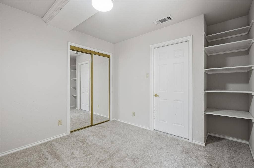 Light gray carpeted flooring, mirrored sliding closet doors, built-in shelving, white paneled door, and recessed lighting