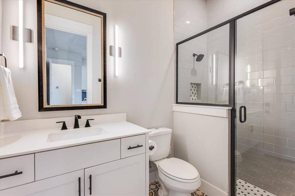 4102 Parkview Boulevard, Celina, TX 75009 Modern bathroom featuring a white vanity with dual drawers and matte black hardware, white quartz countertop, framed mirror with integrated lighting, and a walk-in shower with subway tile surround and frameless glass enclosure
