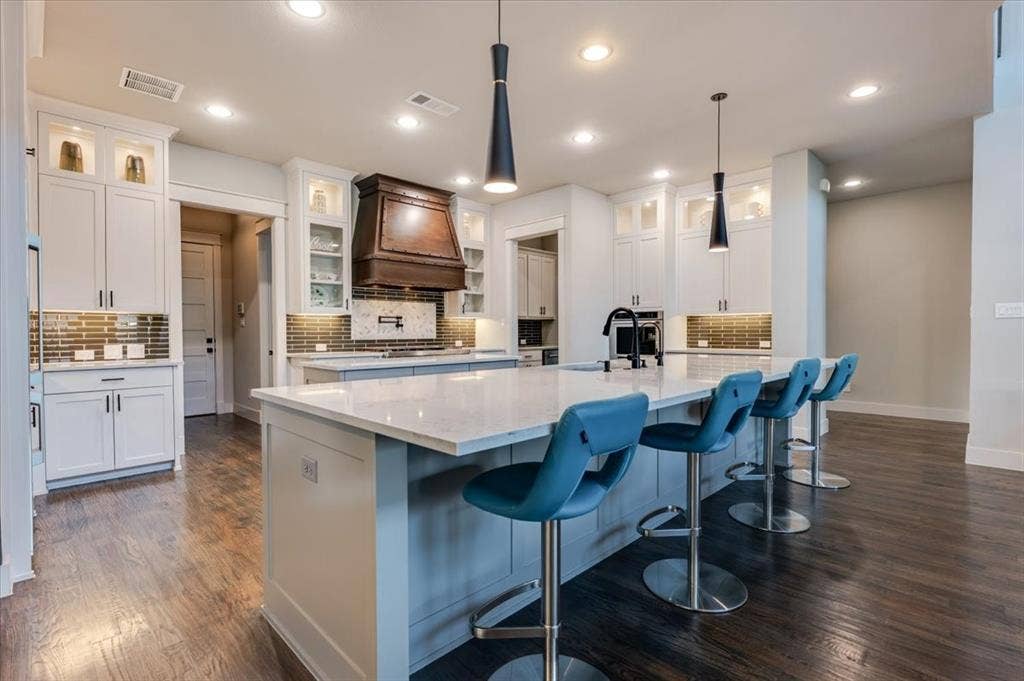 4102 Parkview Boulevard, Celina, TX 75009 Spacious kitchen featuring an expansive central island with a light-toned countertop, white cabinetry with display lighting, a tiled backsplash, and wood-finish flooring