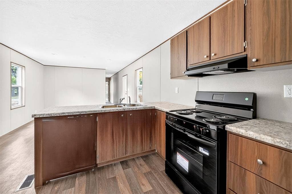 Kitchen featuring wood-finish cabinetry, stone-patterned laminate countertops, integrated black range, black range hood, and wood-finish flooring