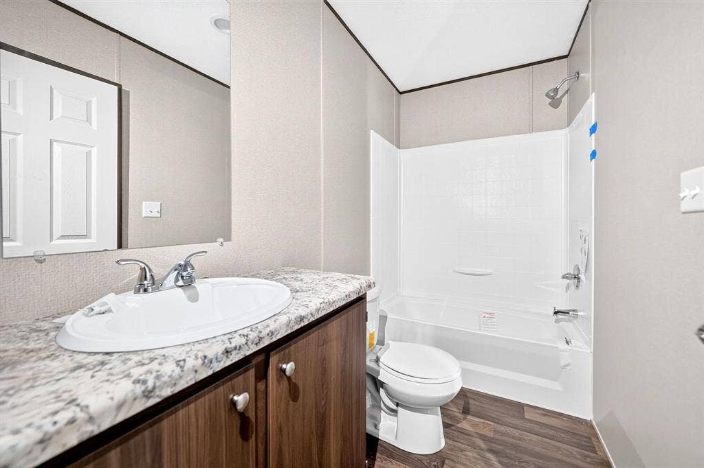 Bathroom featuring a wood-finish vanity, stone-patterned countertop with an integrated basin, wood-finish flooring, and a shower-tub combination with a white surround