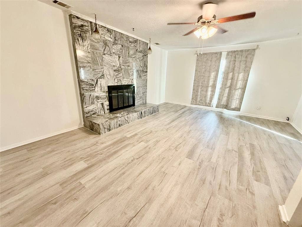 Spacious interior with light wood-finish flooring, a stone-clad fireplace with hearth, and a ceiling fan with integrated lighting