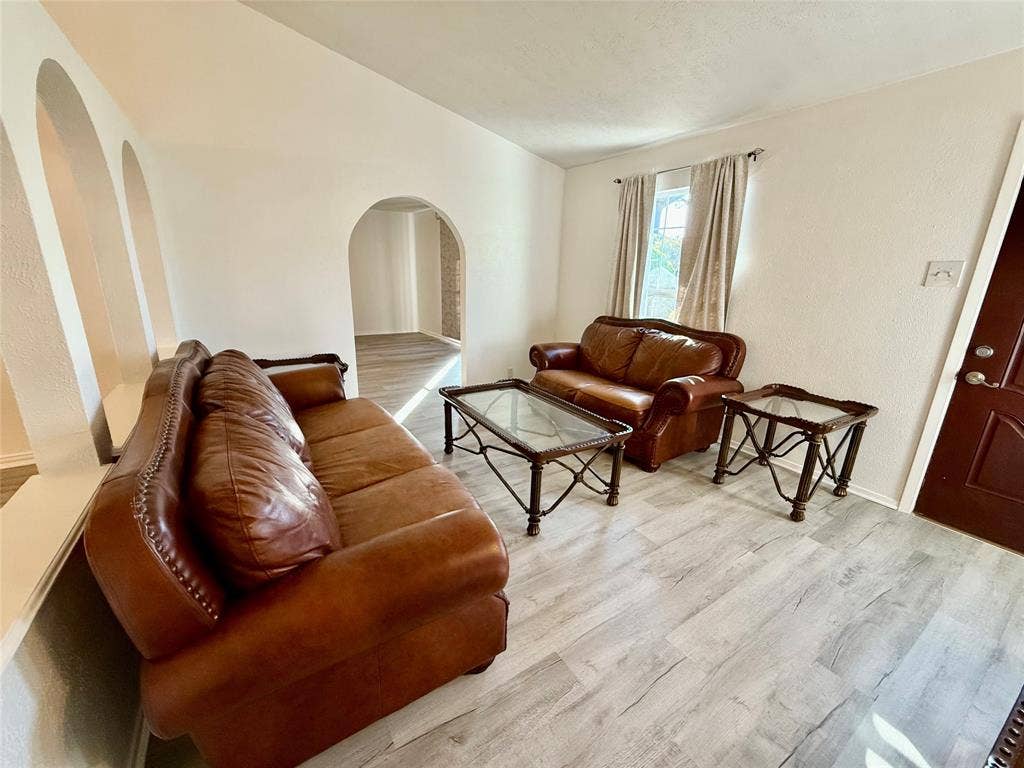 Light wood-finish flooring throughout, arched wall cutouts, and a window with curtain rods