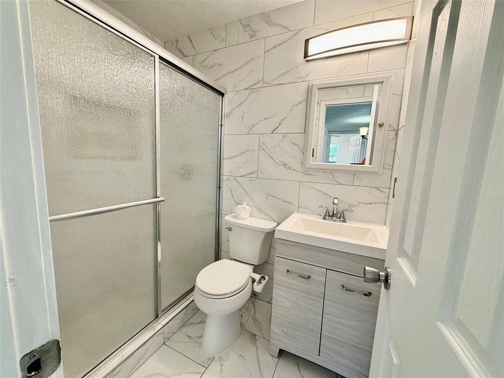 Full-height tiled walls featuring a white marble-look pattern, white vanity with integrated sink, chrome faucet, and a sliding glass shower enclosure