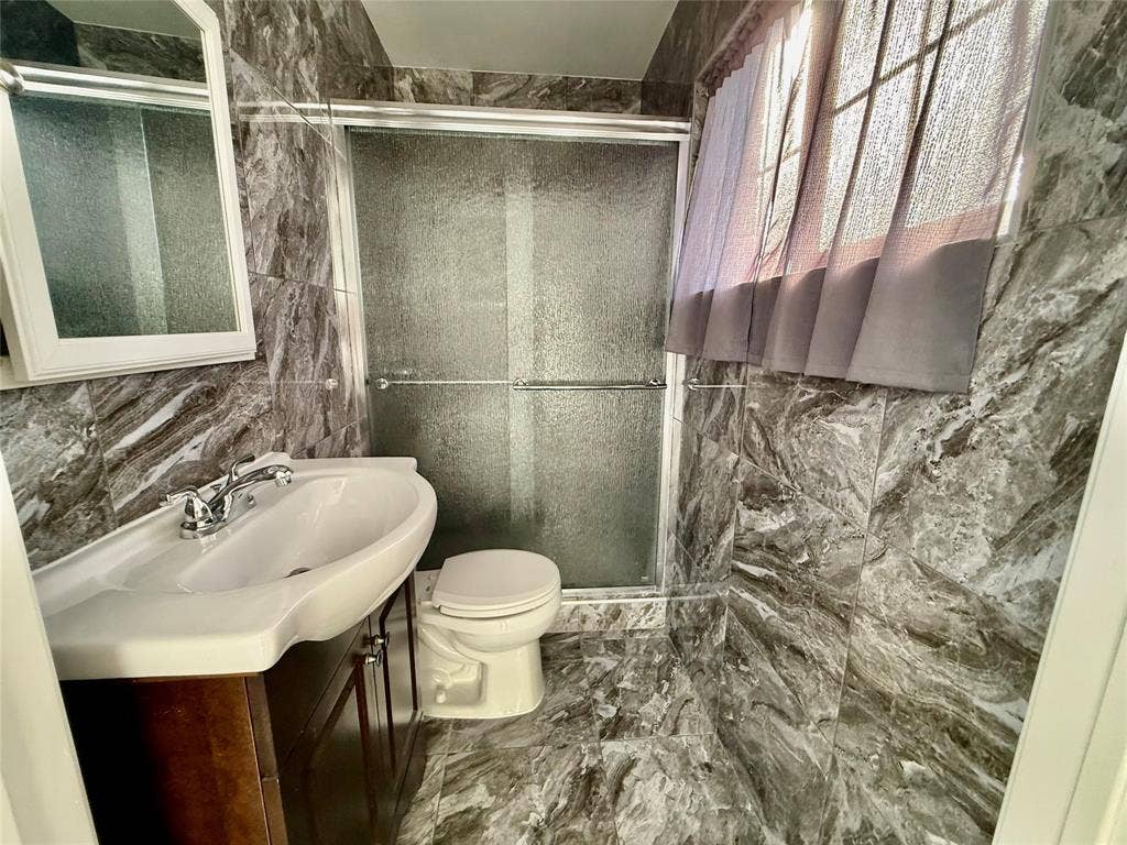 Tiled walls and flooring, wood-finish vanity with an integrated sink, polished chrome faucet, and a sliding glass shower enclosure