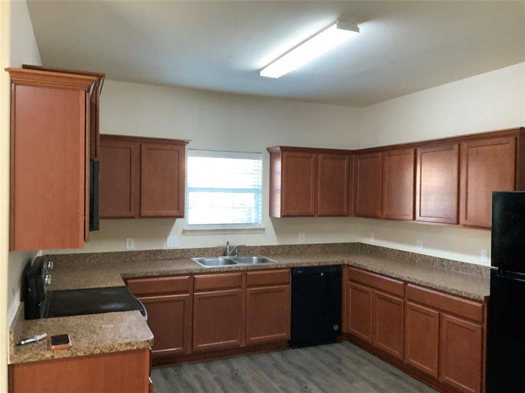 1030 Stanwyck Avenue, Duncanville, TX 75137 U-shaped kitchen featuring wood-finish cabinetry, speckled countertops, stainless steel double basin sink, black built-in dishwasher, and wood-finish flooring