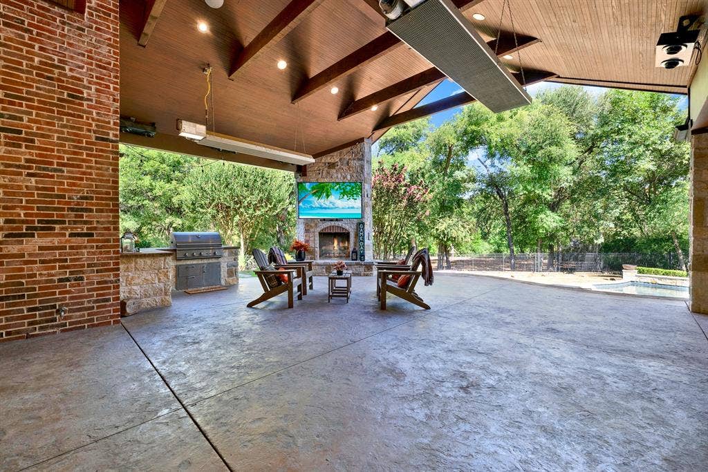 5237 SKY LAKE Drive, Plano, TX 75093 A stacked-stone outdoor fireplace hearth stands beneath exposed wood ceiling beams, framing sweeping views of the lush yard. Warm autumn evenings draw family outside to unwind by a crackling fire as dusk settles.