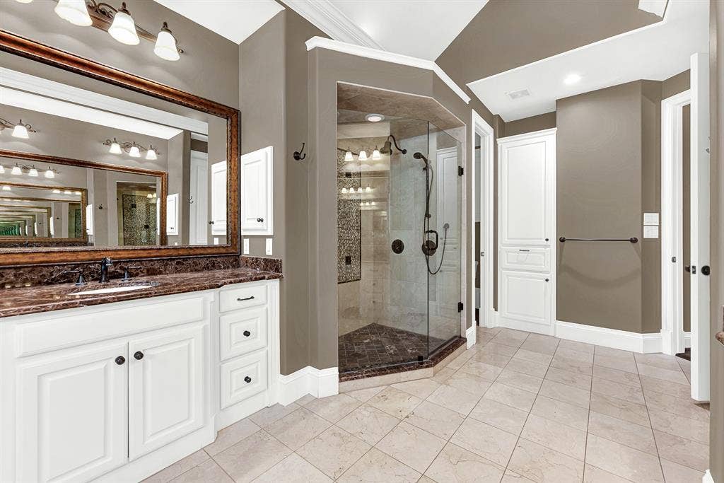5237 SKY LAKE Drive, Plano, TX 75093 An angled, frameless glass walk-in shower showcases custom tilework that reflects brightness across vanity mirrors. Start your day energized under a warm stream of water in this airy space