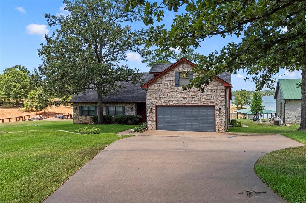 5459 Woodland Shores Drive, Log Cabin, TX 75148 Inviting stone and wood exterior with mature trees and expansive front yard. Two car attached garage plus long driveway for ample parking.
