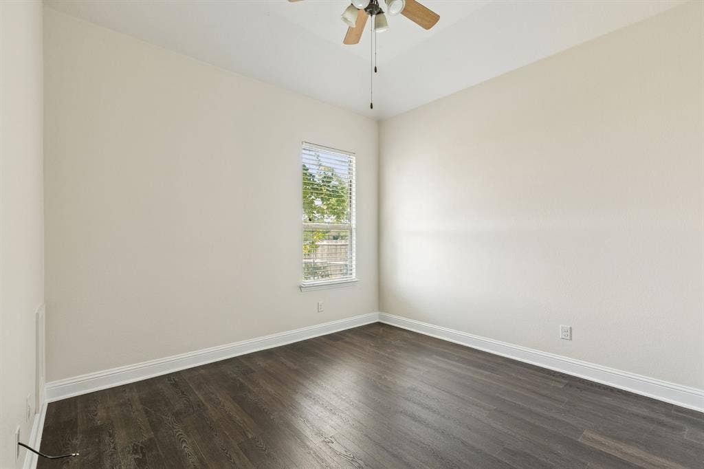 Wood-finish flooring with white trim, a single window, and a ceiling fan with integrated lighting
