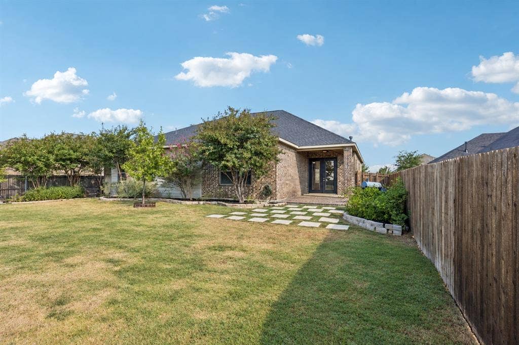 Expansive grassy backyard featuring a full privacy fence, brick exterior, and a stone paver patio