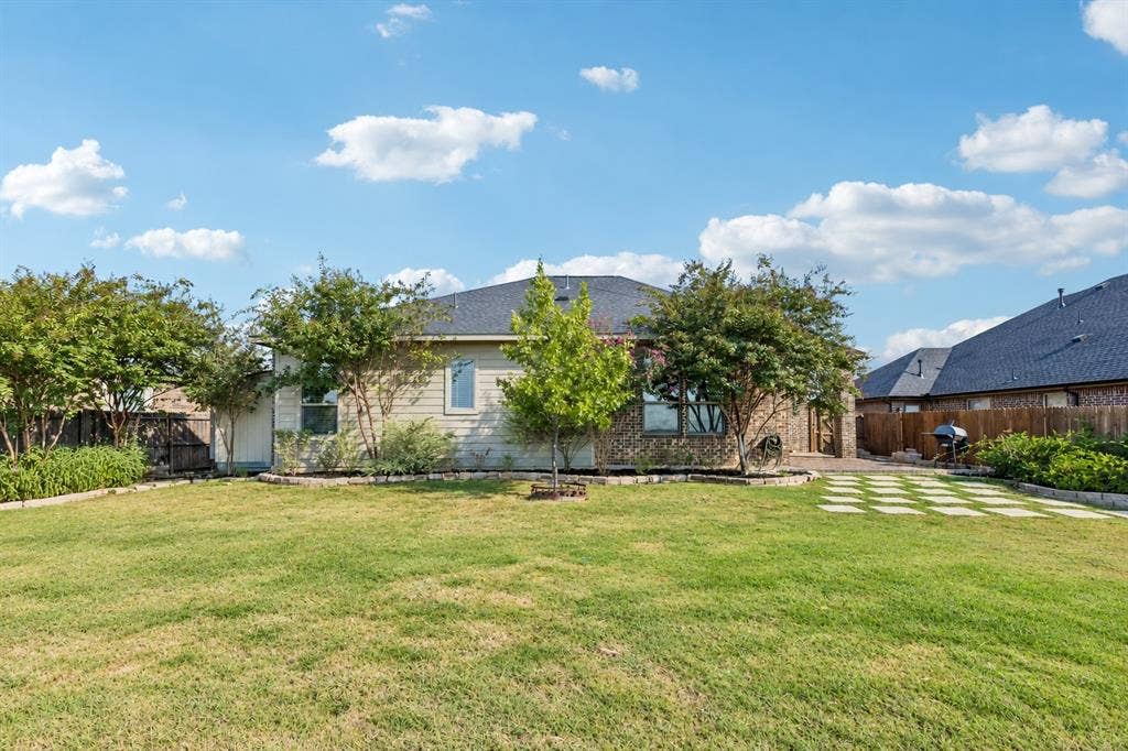 Expansive backyard featuring a manicured lawn, landscaping beds with mature trees, and a stone paver patio